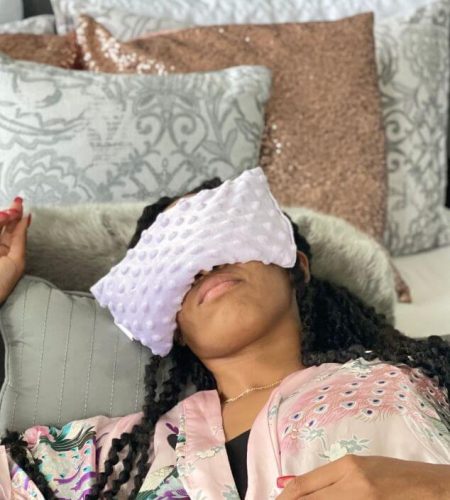 Woman resting on a couch wearing a Mumu Wraps natural eye mask in a cozy home setting