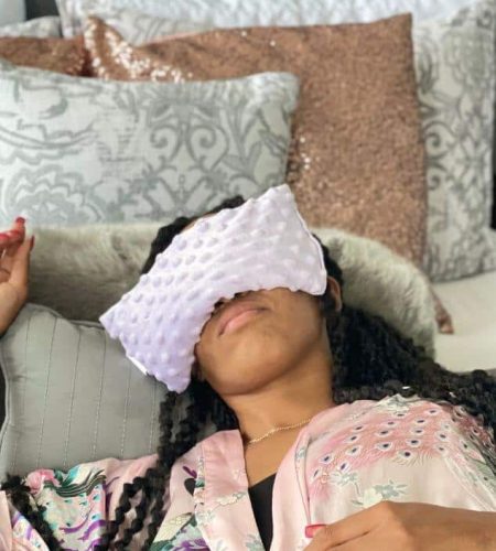 Woman resting on a couch wearing a Mumu Wraps natural eye mask in a cozy home setting