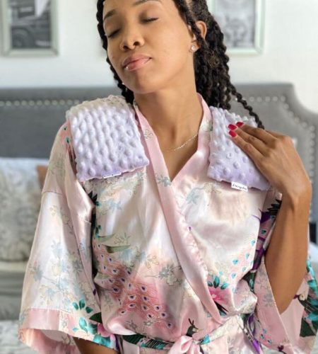 Person wearing a lavender shoulder heating pad by Mumu Wraps in a cozy bedroom setting